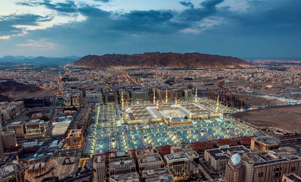 A stunning aerial view of Al-Masjid an-Nabawi in Medina at dusk, showcasing its illuminated grandeur.
